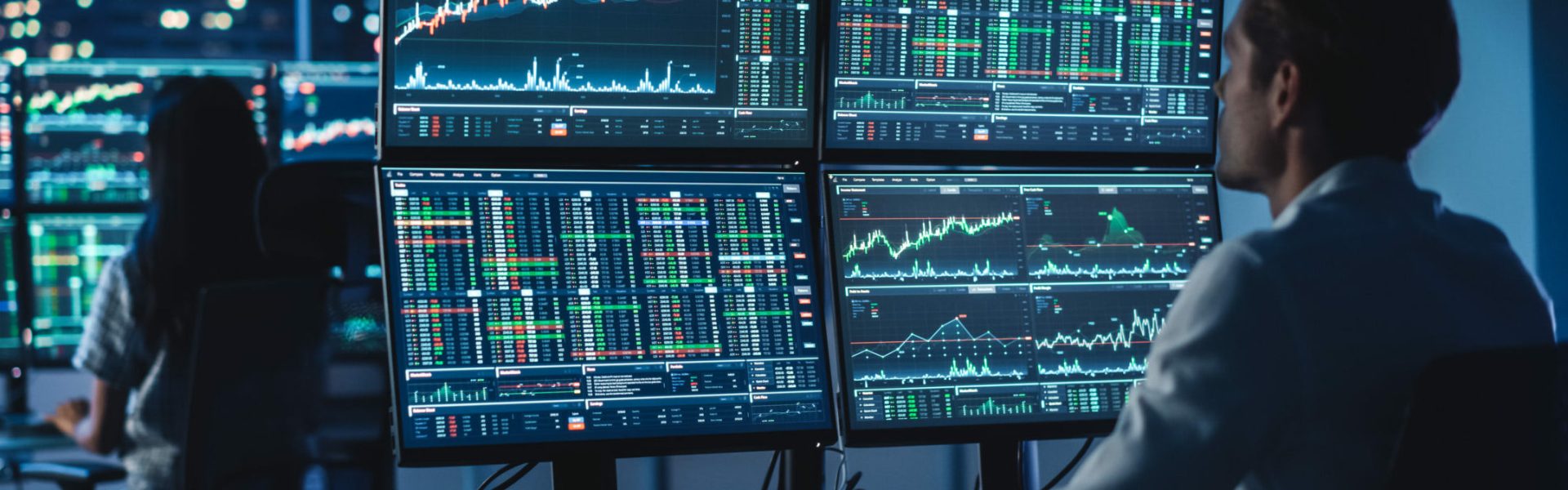 Financial Analyst Working on a Computer with Multi-Monitor Workstation with Real-Time Stocks, Commodities and Foreign Exchange Charts. Businessman Works in Investment Bank City Office at Night.