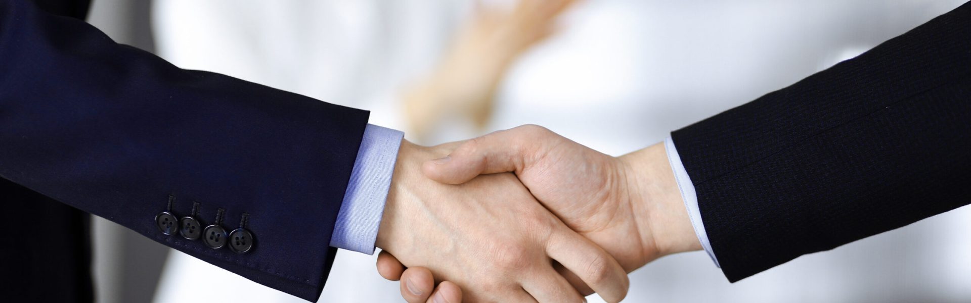 Business people shaking hands at meeting or negotiation, close-up. Group of unknown businessmen and a woman standing in a modern office. Teamwork, partnership and handshake concept.